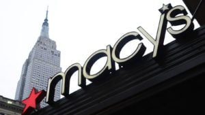 Macy's (M) logo on storefront in city with white sky behind. retail stocks