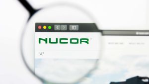 A magnifying glass zooms in on the Nucor (NUE) website. 