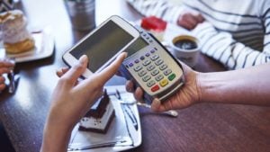 a person holding a smartphone over a checkout scanner representing payment shares to buy