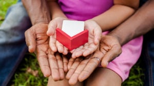 Hands of family together holding house in green park.