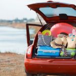 a red car on a beach has the trunk open and overflowing with suitcases and beach gear