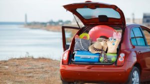 a red car on a beach has the trunk open and overflowing with suitcases and beach gear
