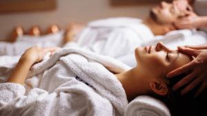 Photo of a woman and man in white robes, laying down relaxing at a spa (penny stocks)