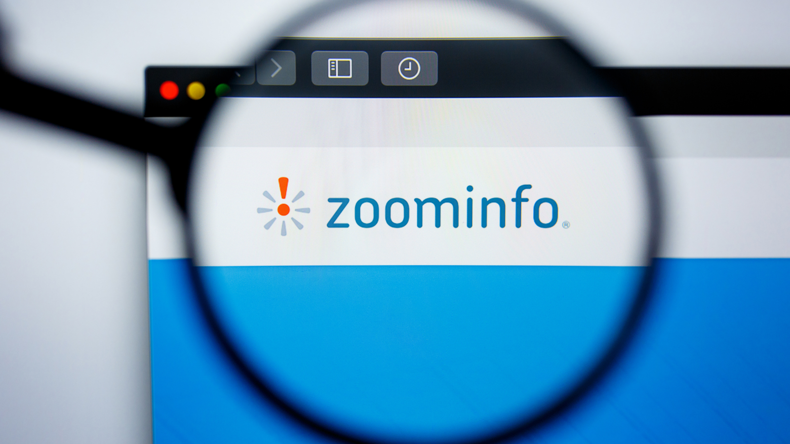 A magnifying glass zooms in on the ZoomInfo (ZI) logo