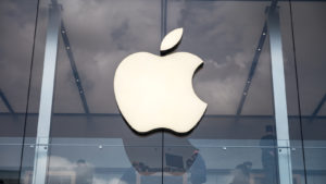 White Apple (AAPL stock) logo on glass with people in background