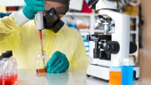 a scientist with protective equipment and microscope in a lab representing VYNE Stock. 