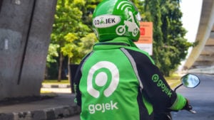 A Gojek driver in company helmet and jacket waits at a stoplight.