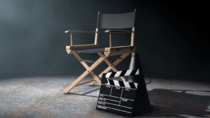 A director's chair, megaphone and movie clapper are arranged in a dramatically lit room.