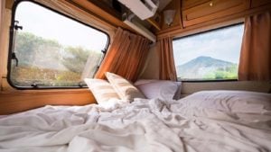 The inside of a camper van with a bed and two windows looking outside.