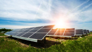 Solar energy panels are arranged in a green field under a sunny sky.