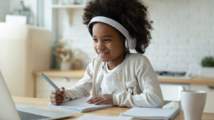 a girl sitting in front of a laptop working on homework. investing for kids