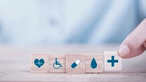 A close-up shot of a hand choosing wooden blocks with emoticons related to health insurance.