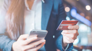 A woman uses her phone and credit card to make a payment.