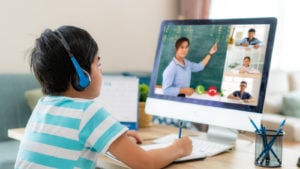 a child takes notes while attending an online class. represents education stocks