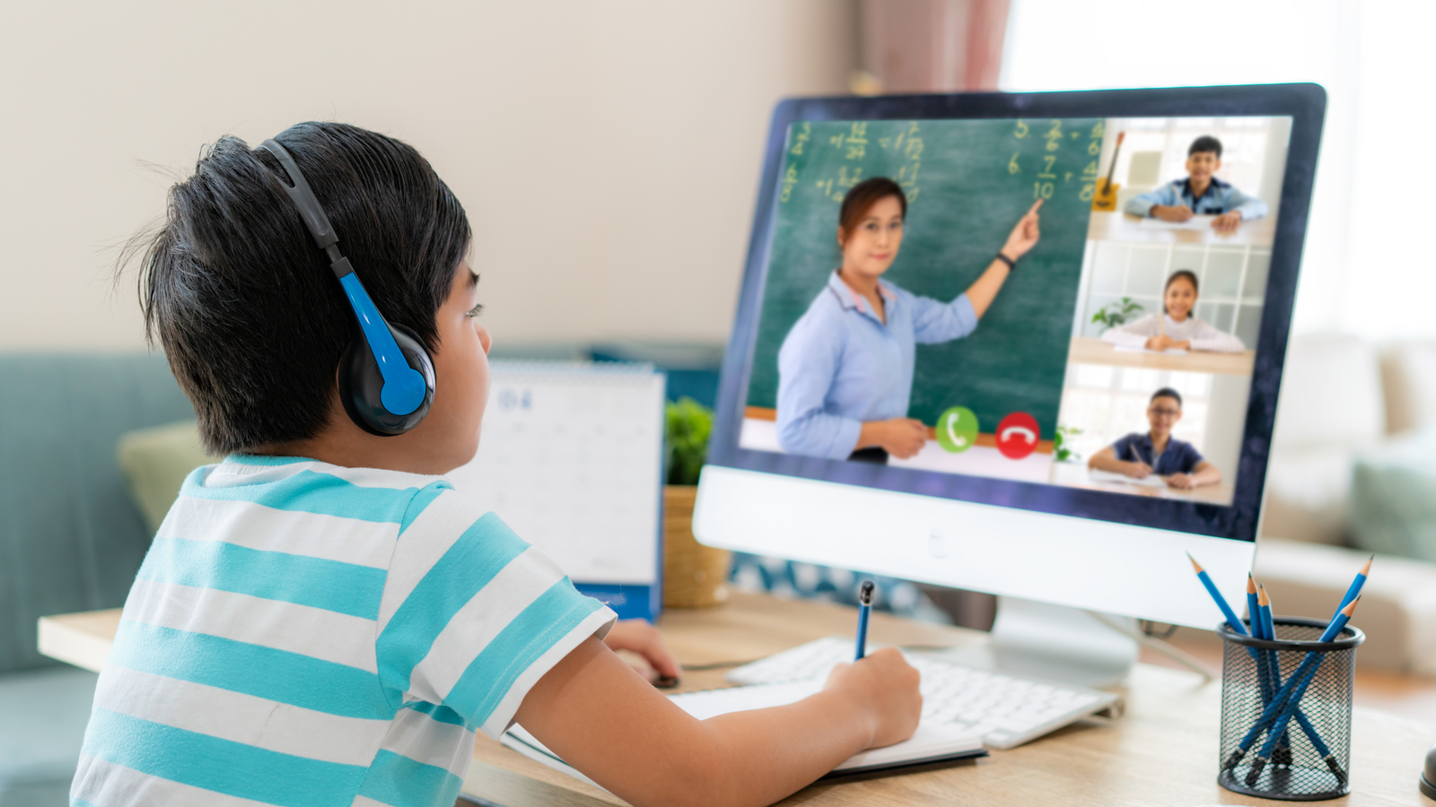 a child takes notes while attending an online class. represents EDU stock.