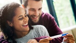 A youthful couple smiles while holding a pregnancy test.