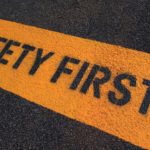Safety First painted on a yellow caution strip on dark pavement. safest stocks for portfolio stability. safe stocks