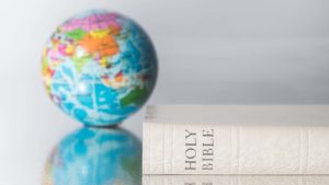 A white Holy Bible lays on its side next to a small globe. 