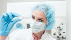 A scientist holding up her biotech experiment in a small Petri dish.