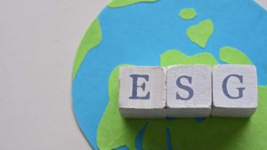 Wooden blocks spell out "ESG" over a flat illustration of the earth.