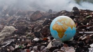 An intact globe is surrounded by a pile of garbage and burning waste. to represent esg stocks