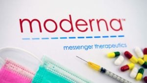 The Moderna (MRNA) logo surrounded by syringes, pills and disposable face masks. 