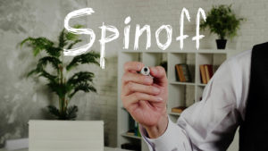 A hand holds a marker in an office under the word "Spinoff."