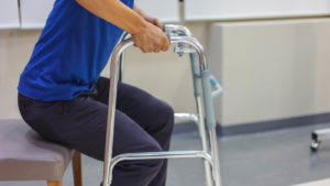 A man using a walker, about to stand from a chair.