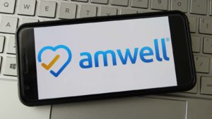 The logo for American Well (AMWL) displayed on a smartphone screen. The smartphone rests on top of a keyboard.