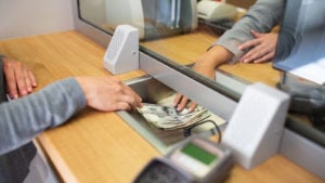 bank customer sliding money to teller at bank desk representing Financial Stocks.