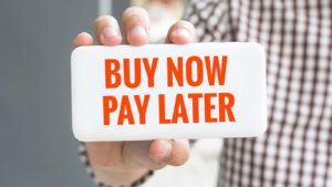 A close-up shot of a hand holding a sign that reads "Buy Now, Pay Later."