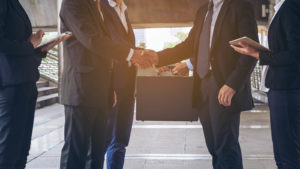 two businessmen shaking hands with peers at their side