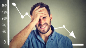 Man holding head with a falling chart in the background.