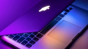 An Apple MacBook Air laptop sitting under bright purple lights.