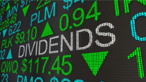 stock market ticker screen with the word "dividends" appearing in large text representing Which Stocks Pay Dividends.