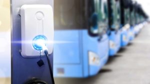 A close-up shot of an electric vehicle charging station with a row of electric buses in the background representing LEV stock.