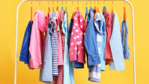 colorful clothes on a white rack with a bright yellow background representing DBGI stock.