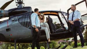 Two individuals step out of a helicopter while the pilot stands nearby.