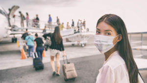 A photo of a woman in a face mask waiting to board an airplane.
