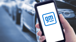 Image of the new GM logo on a smartphone with cars in the background.