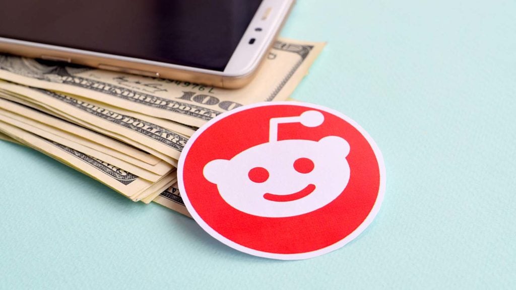 A Reddit sticker rests next to an iPhone and a pile of cash.