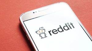 The Reddit app and logo displayed on a smartphone screen representing AMC, GME and Meme Stocks