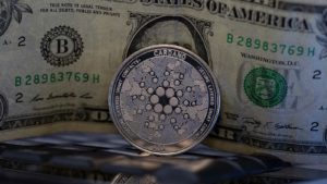 A Cardano (ADA) going in front of a dollar bill.