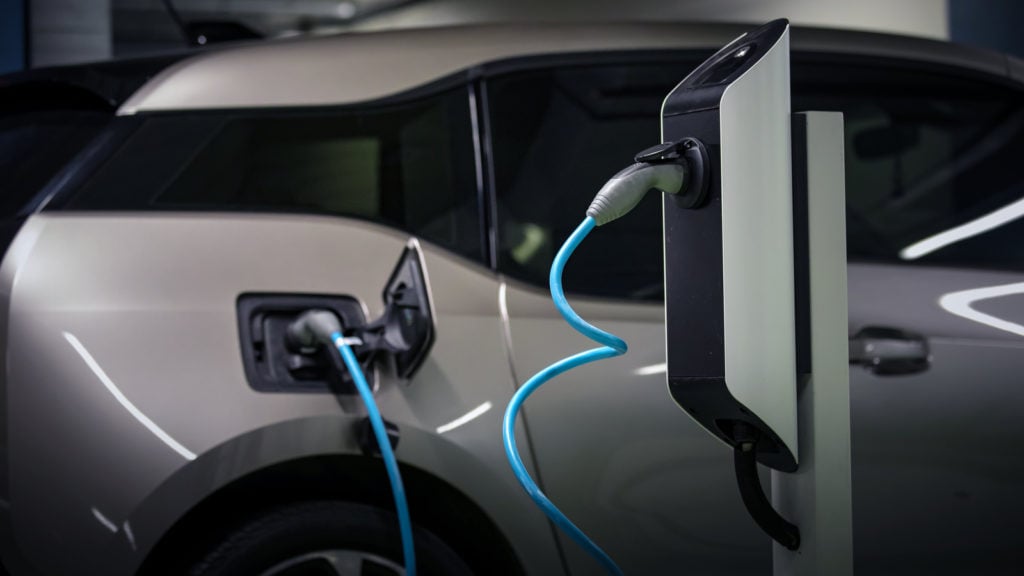 Image of a grey electric vehicle plugged in at a charging station.
