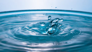 An enlarged photograph of a drop of water falling onto a container with a water surface.