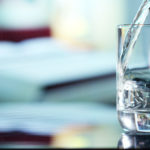 A photo of water being poured into a glass that's sitting on a table.