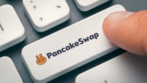 A finger hovers over a white keyboard key that says "PancakeSwap" with the CAKE logo.