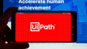 The UiPath logo on a smartphone in front of a computer screen. Cathie Wood Stocks