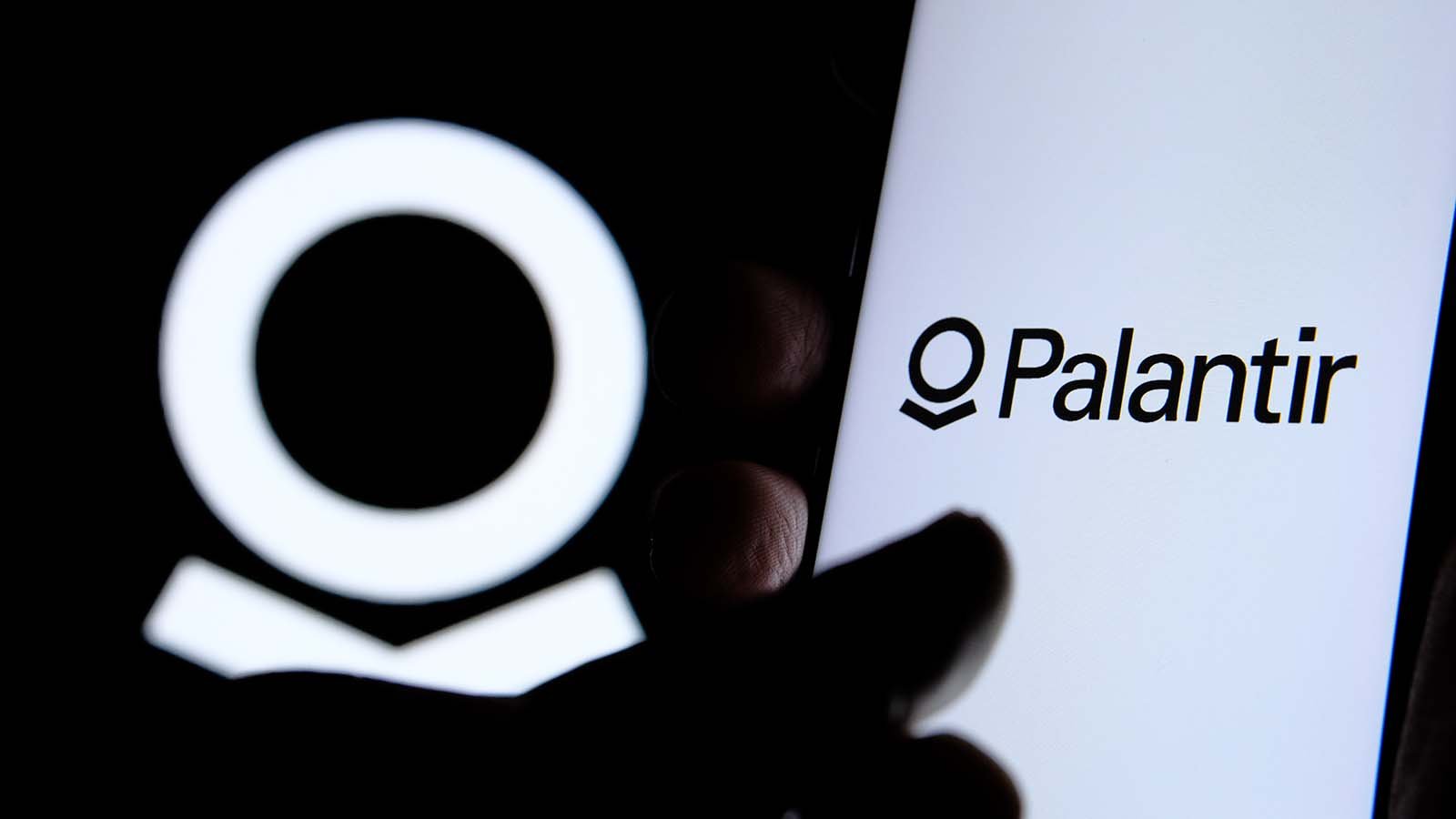 A close-up shot of a hand on a screen with the Palantir (PLTR) logo.