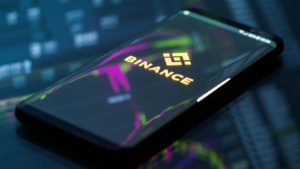 The Binance logo on a smartphone with a neon chart in the background representing Binance Crypto News.